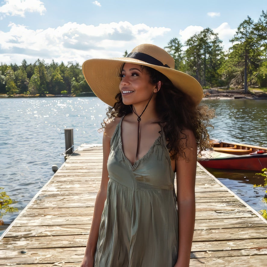 Woman wearing a wide brim damazo beige hat standing on a wooden dock by a lake.
