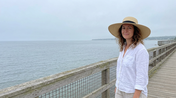 Woman with wavy hair wearing a silk-lined straw sun hat on a seaside boardwalk